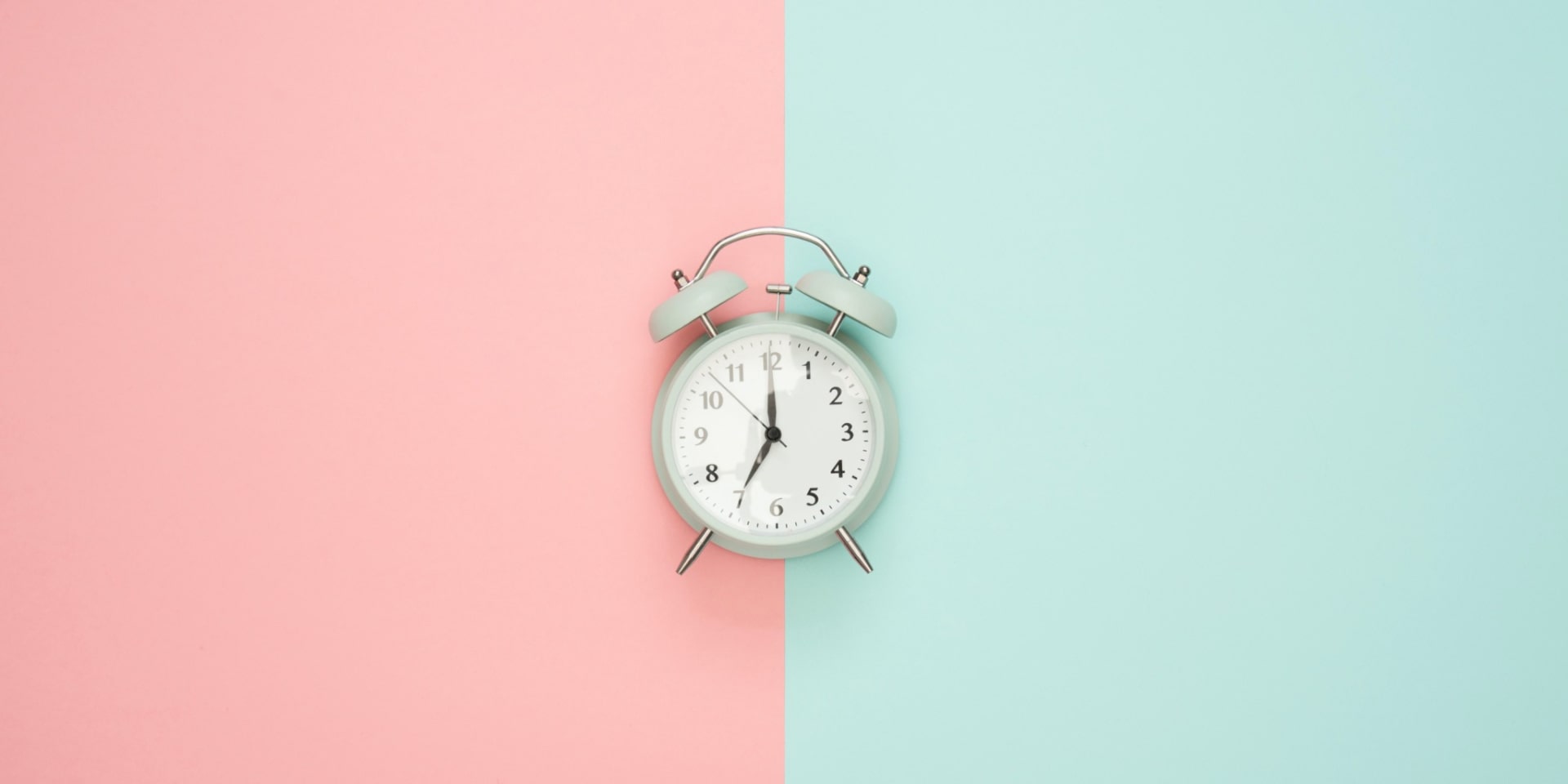 An alarm clock placed in the middle on a pink and green visual background.