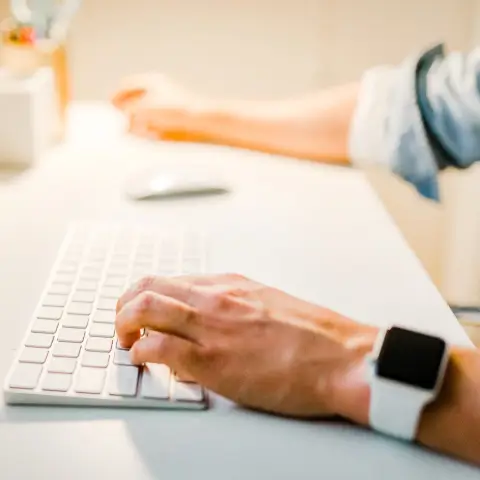 A hand wearing an Apple Watch typing on a keyboard