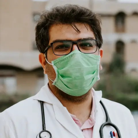 A doctor wearing a stethoscope and looking into the camera