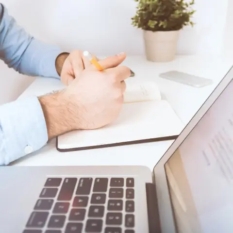 A doctor writing in a notebook next to a laptop