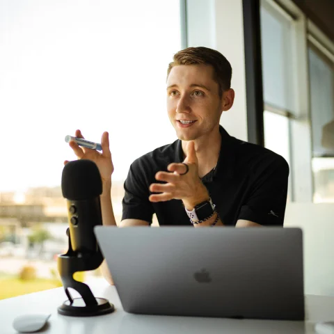 A podcaster interviewing someone off camera with microphone and laptop